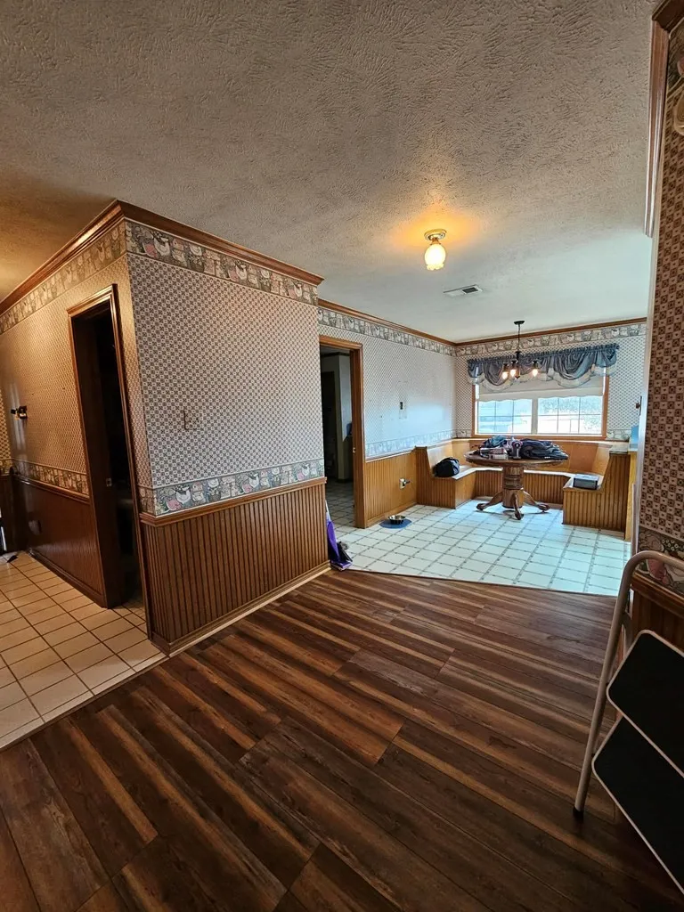 Dining space featuring a wainscoted wall, wallpapered walls, wooden walls, light wood finished floors, and a textured ceiling