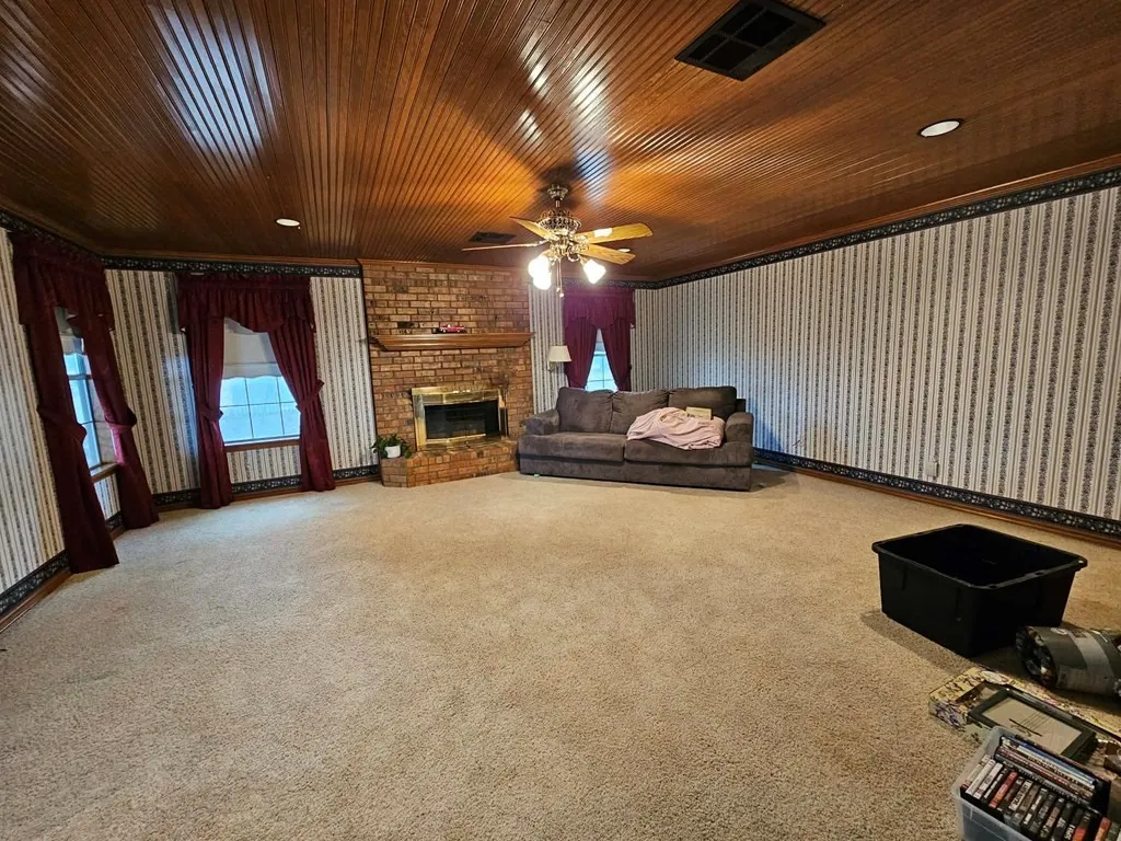 Unfurnished living room featuring carpet, a brick fireplace, and ceiling fan