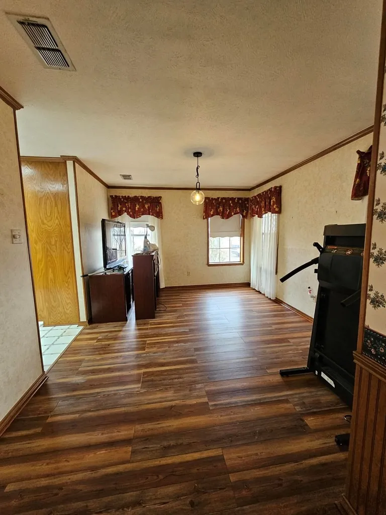 Unfurnished dining area with dark wood-style flooring, crown molding, a textured ceiling, and a textured wall