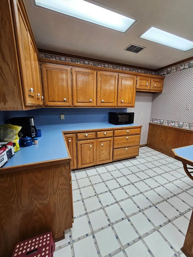 Kitchen featuring wood finish cabinets, wallpapered walls, light floors, light countertops, and black microwave