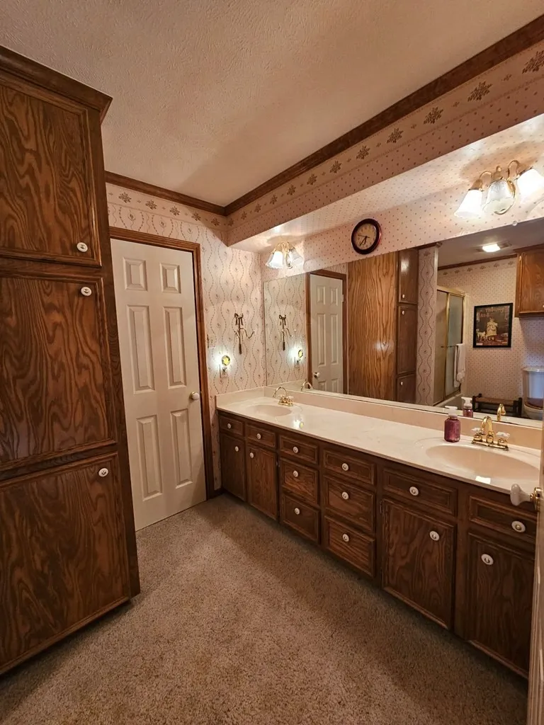 Full bath featuring dark colored carpet, wallpapered walls, double vanity, and a textured ceiling