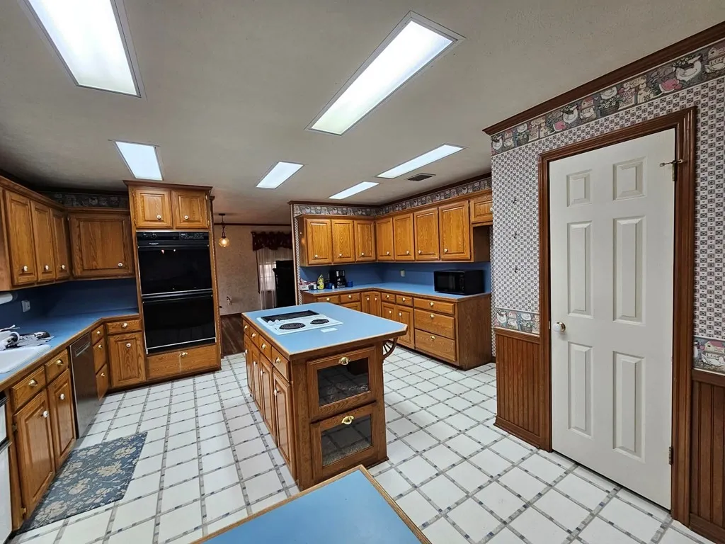 Kitchen featuring wood finish cabinetry, light floors, black appliances, a center island, and wallpapered walls