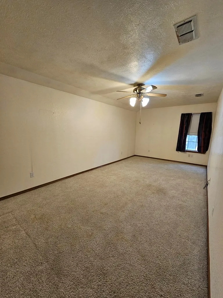 Empty room with light carpet, a textured ceiling, and a ceiling fan