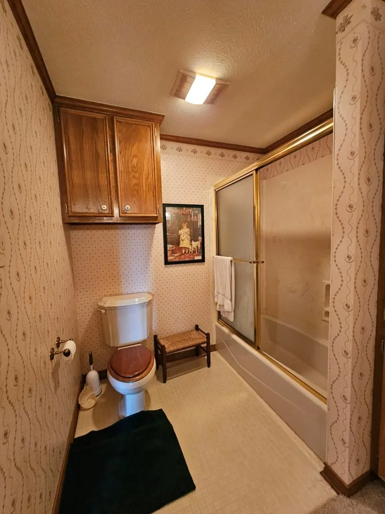 Full bathroom with a textured ceiling, enclosed tub / shower combo, crown molding, and wallpapered walls