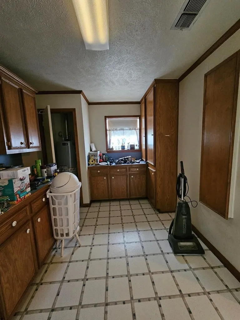 Kitchen with light flooring, crown molding, wood finish cabinets, dark countertops, and a textured ceiling