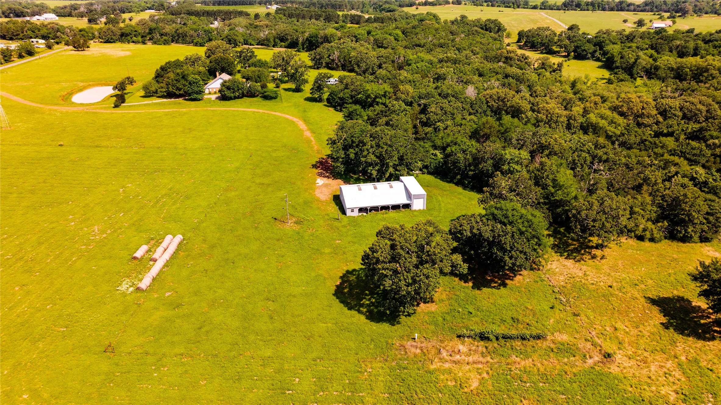 Expansive acreage featuring a white outbuilding with covered outdoor space, a large pond, and mature tree lines