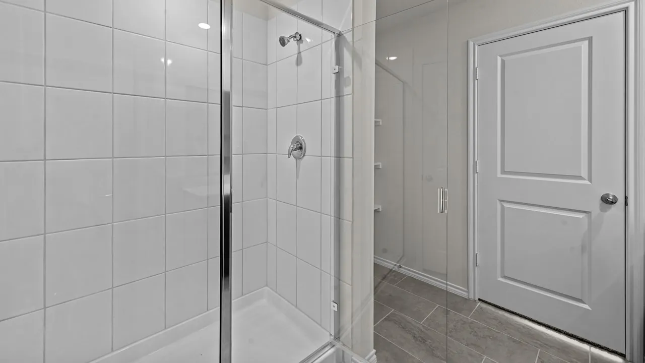 Walk-in shower featuring a chrome shower head and handle, clear glass enclosure, and white square tile walls