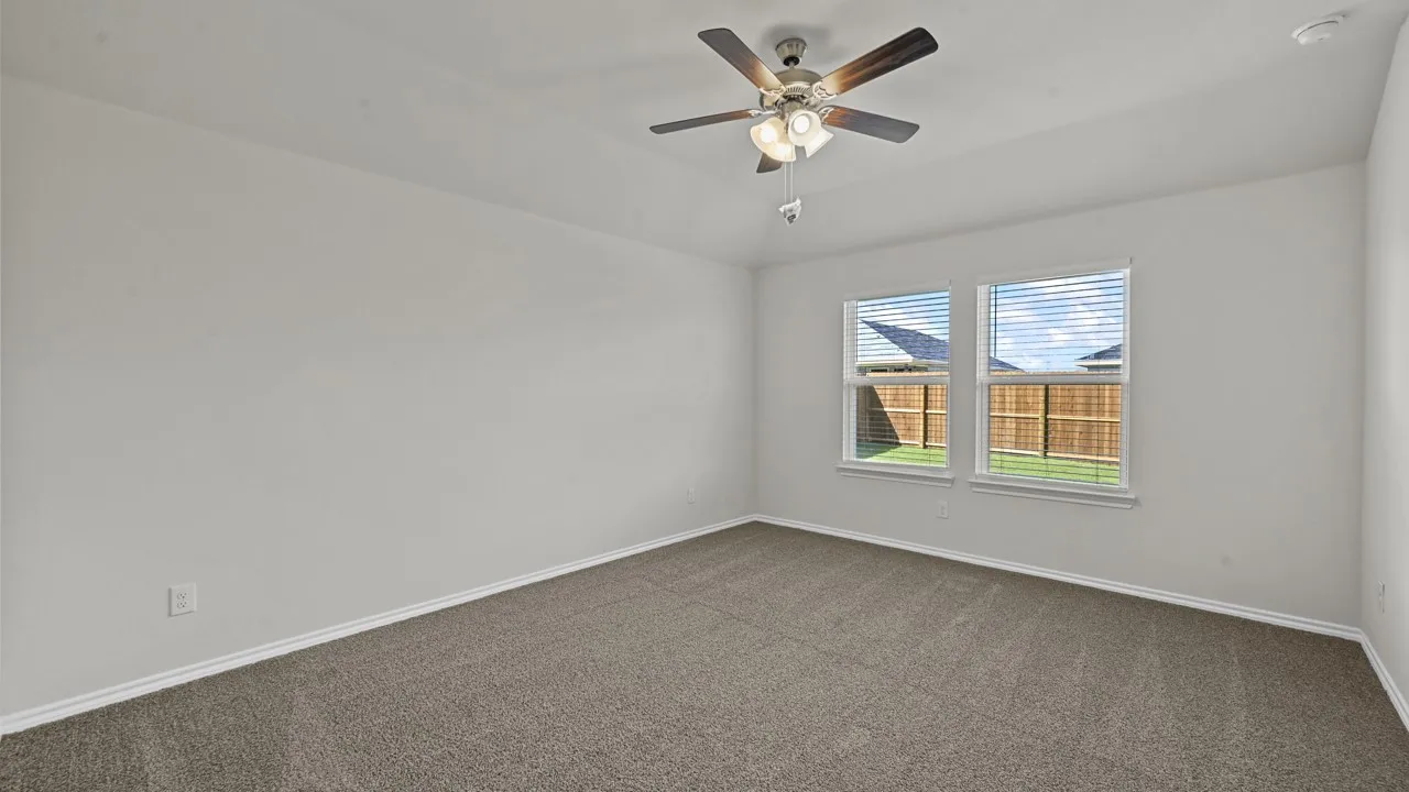 Carpeted interior room featuring a ceiling fan with integrated lighting, two windows with blinds, a tray ceiling, and white baseboards