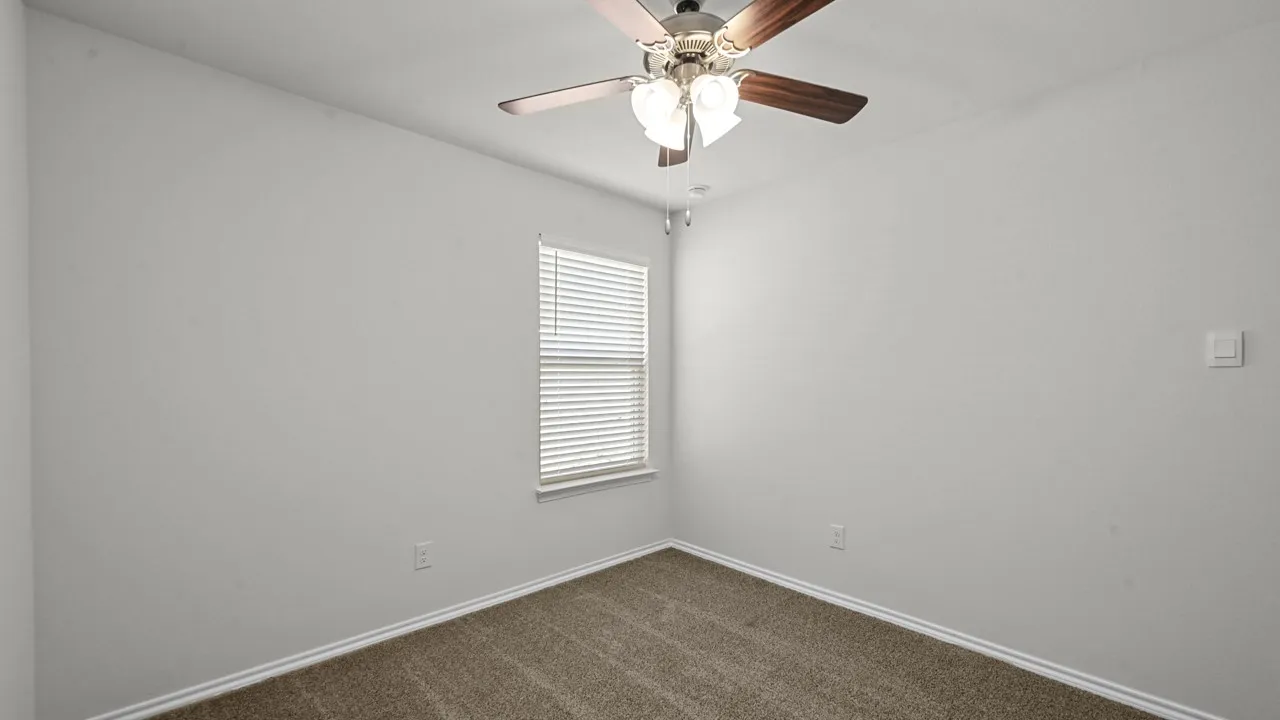 Interior room featuring neutral wall paint, textured carpeting, a single window with horizontal blinds, and a ceiling fan with integrated lighting