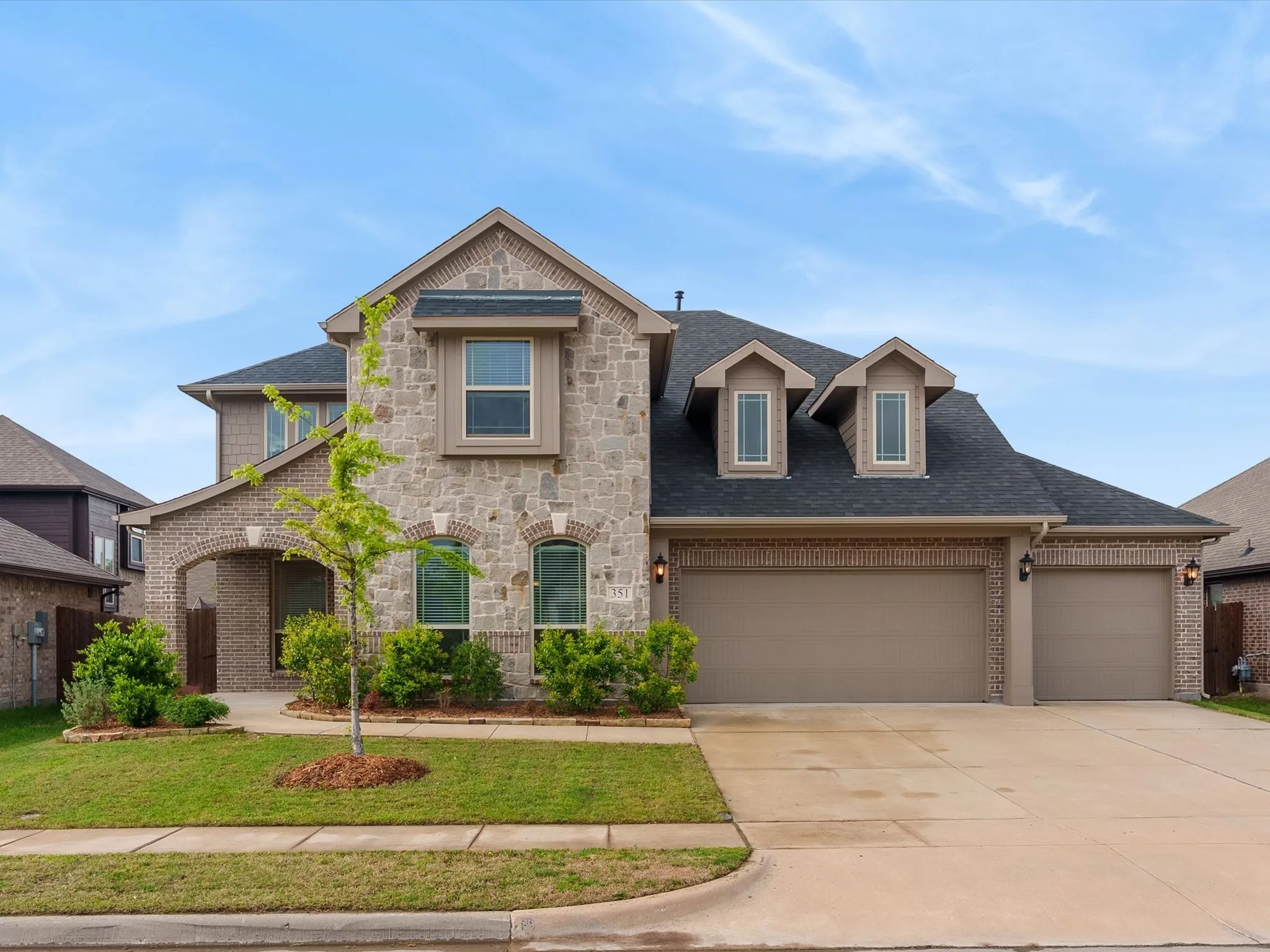 View of front of property featuring a shingled roof, an attached garage, driveway, stone siding, and a front lawn