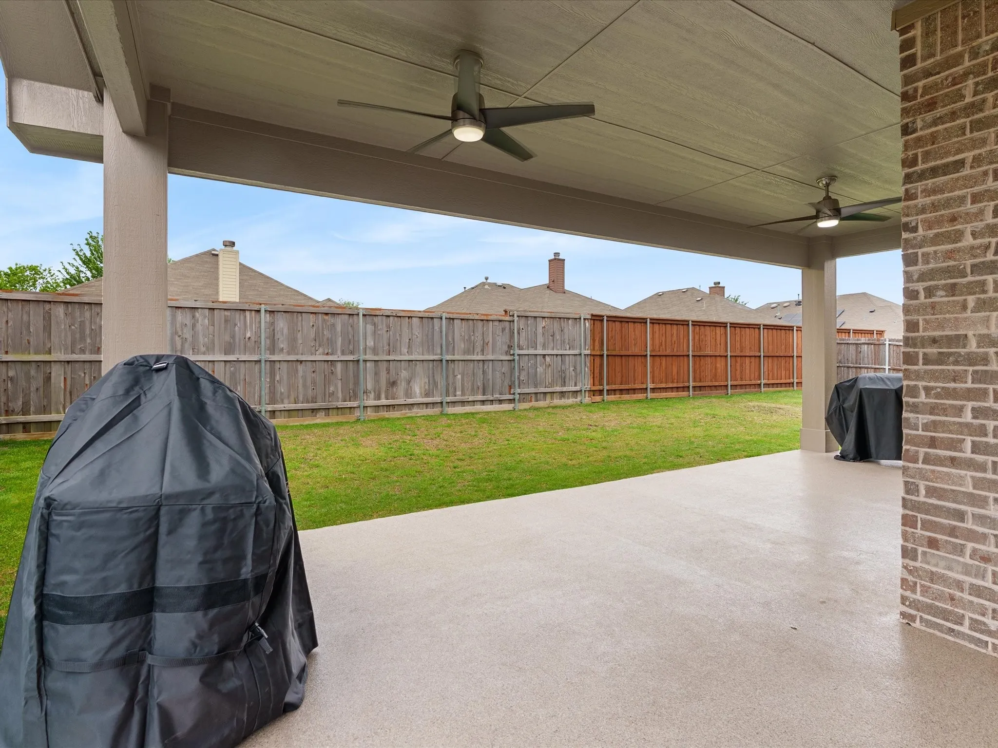 Fenced backyard featuring a ceiling fan, grilling area, and a patio