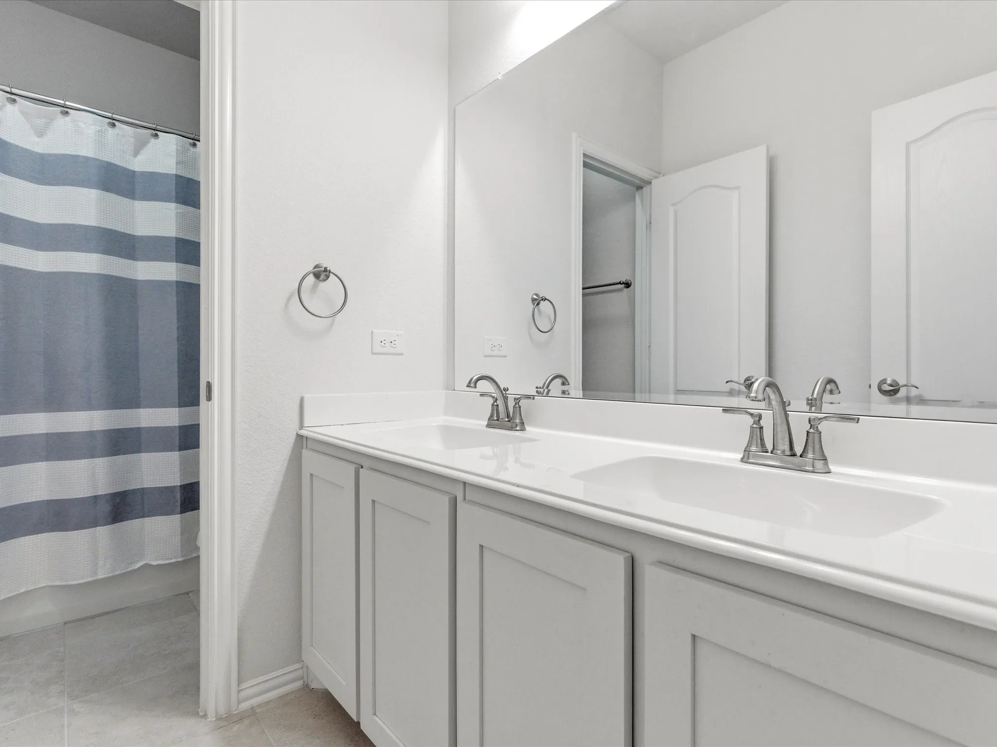 Bathroom featuring double vanity, a shower with shower curtain, and light tile patterned floors