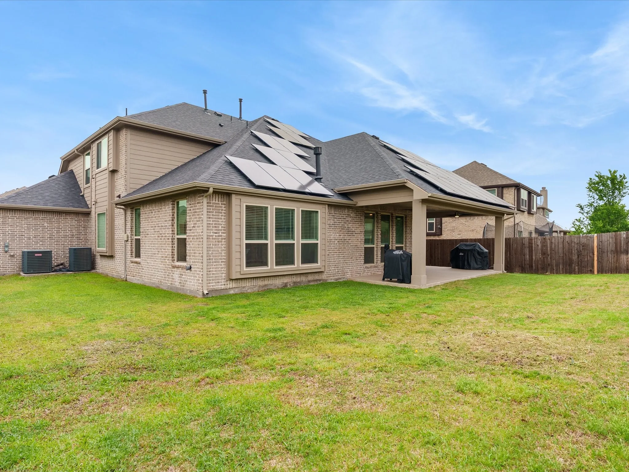 Back of house with brick siding, a patio, roof mounted solar panels, and a fenced backyard