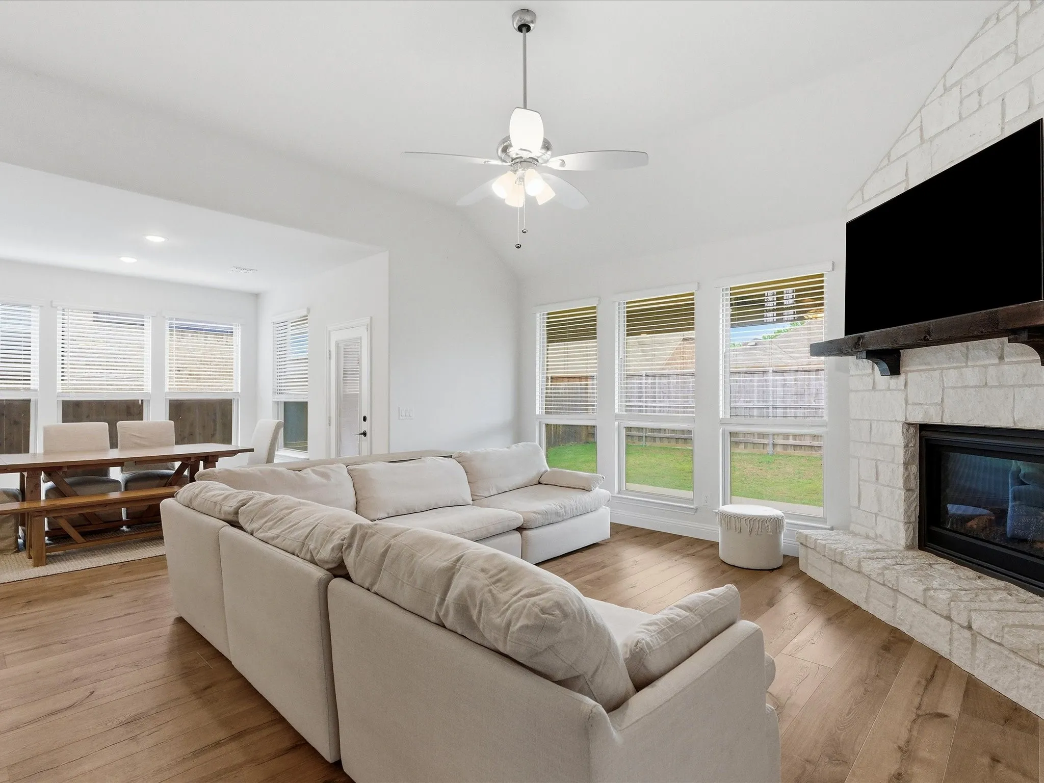 Living area featuring light wood-style flooring, a stone fireplace, lofted ceiling, and a ceiling fan