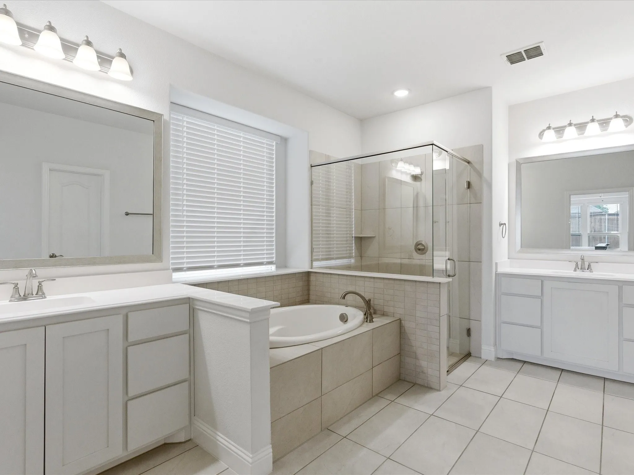 Bathroom featuring two vanities, a stall shower, a bath, and light tile patterned floors