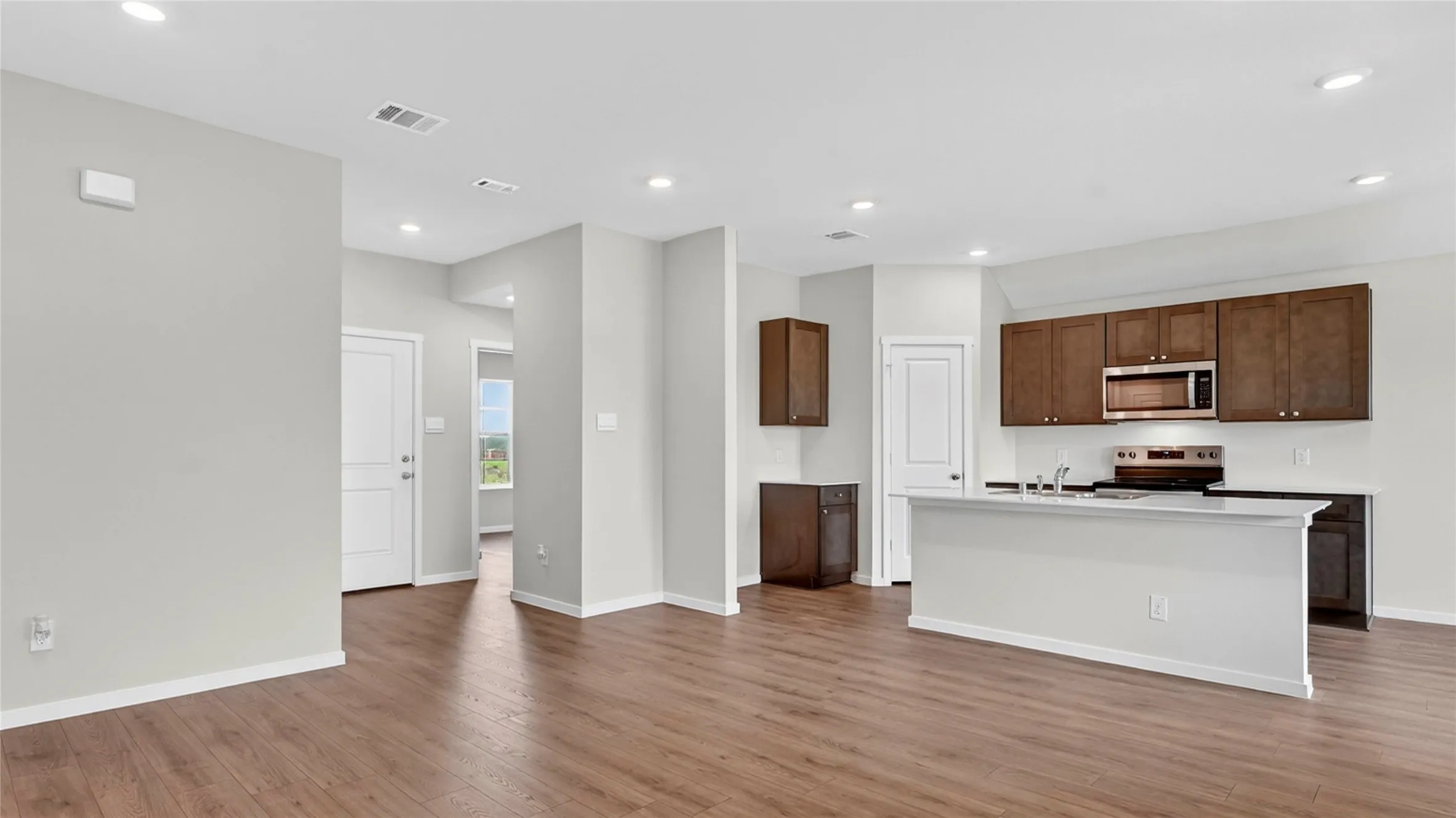 Open-concept living space featuring wood-finish flooring, recessed lighting, and a kitchen with dark wood cabinetry