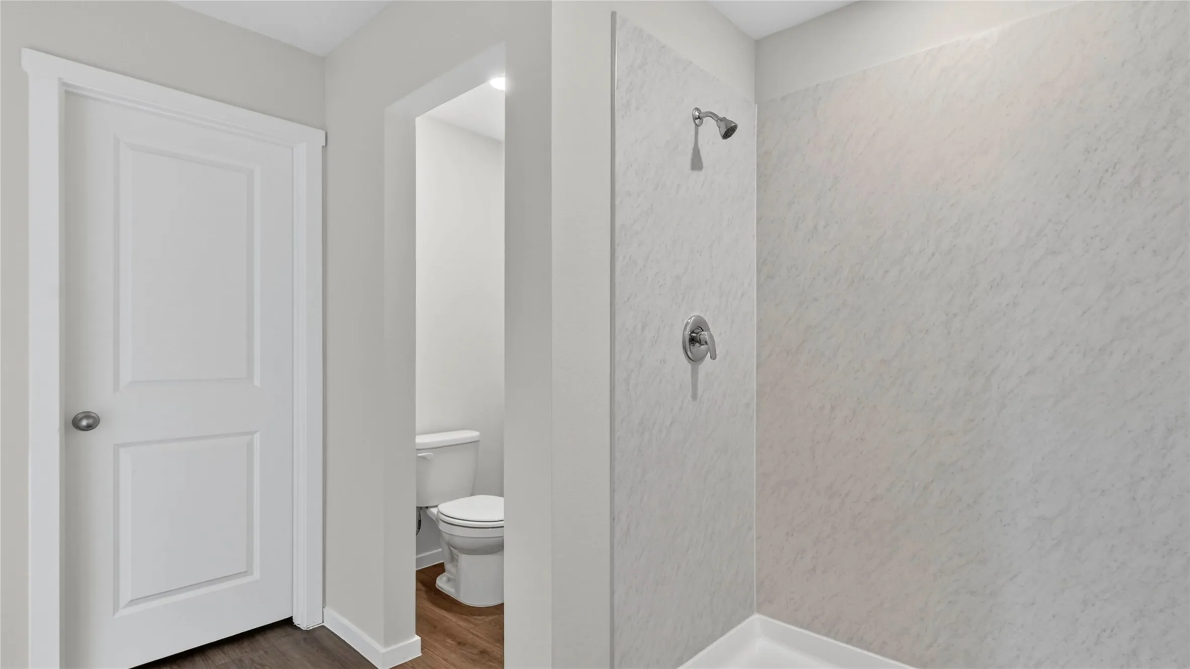 Shower enclosure featuring a chrome shower head and handle, with a separate water closet visible through an open doorway