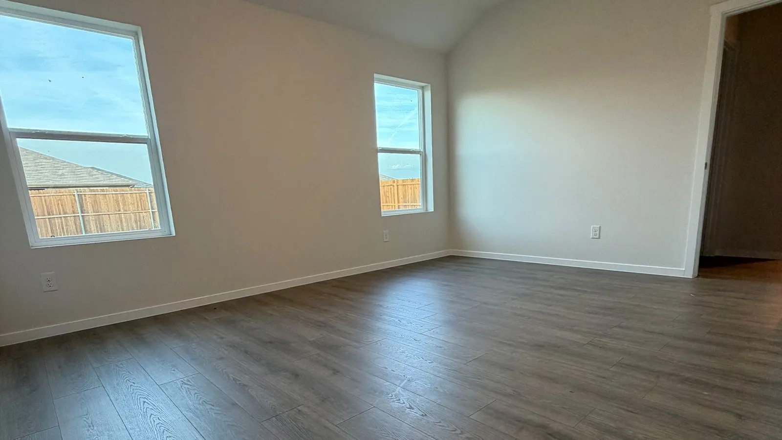 Spare room featuring vaulted ceiling and dark wood-style floors