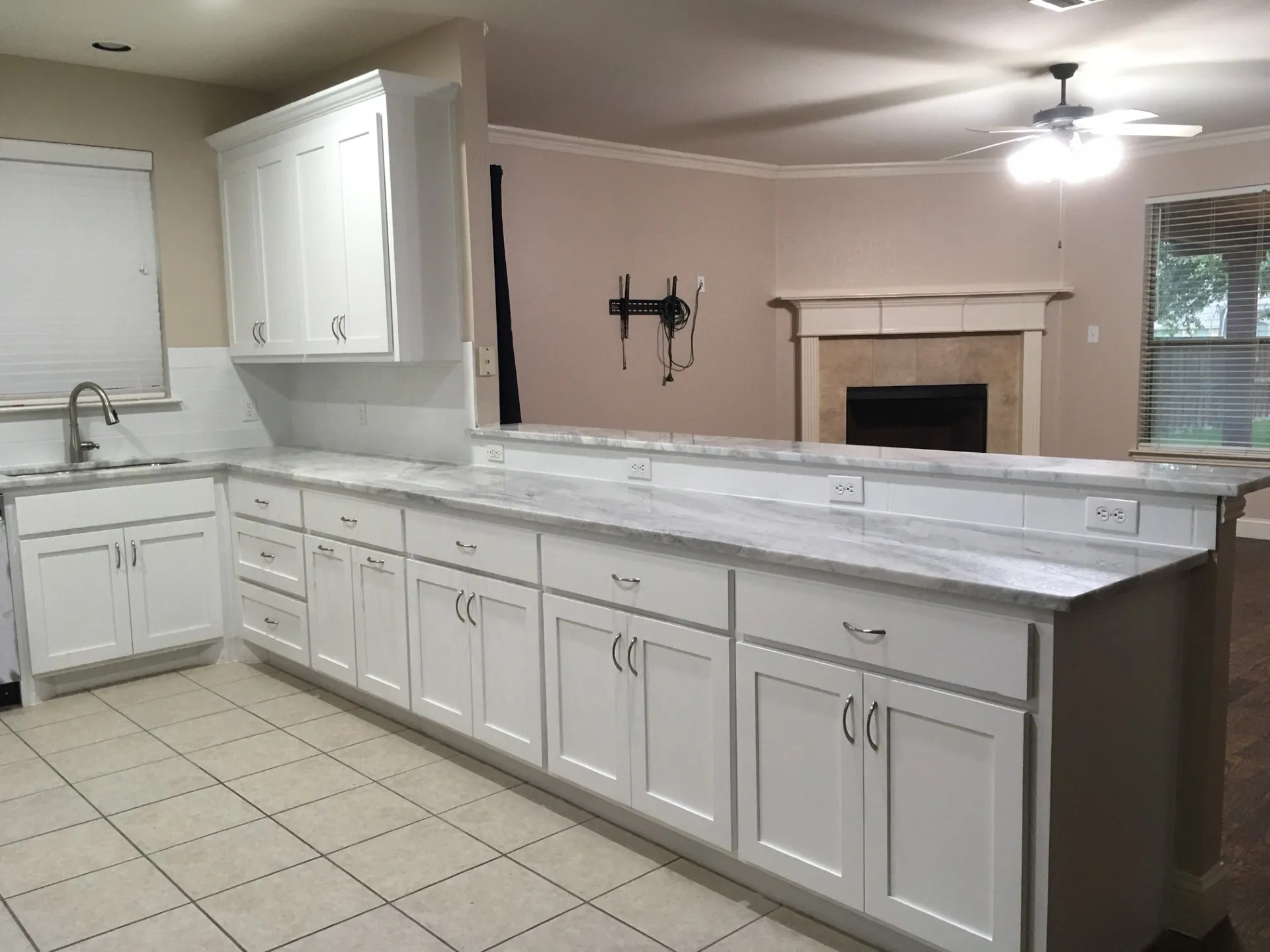 Kitchen featuring white cabinets, a tiled fireplace, light stone countertops, a peninsula, and a ceiling fan