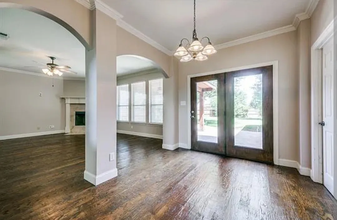 Foyer entrance with dark wood finished floors, ornamental molding, arched walkways, hanging lights, and a fireplace with flush hearth