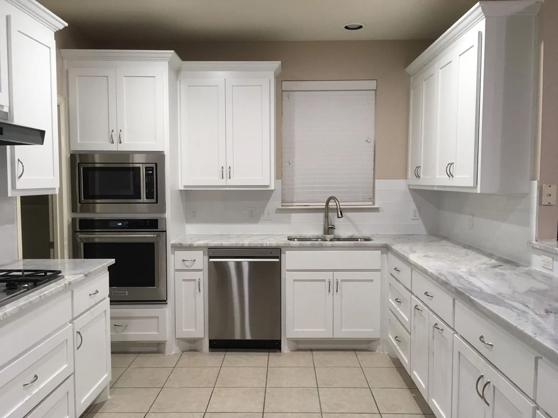 Kitchen featuring stainless steel appliances, white cabinets, light stone countertops, and light tile patterned flooring