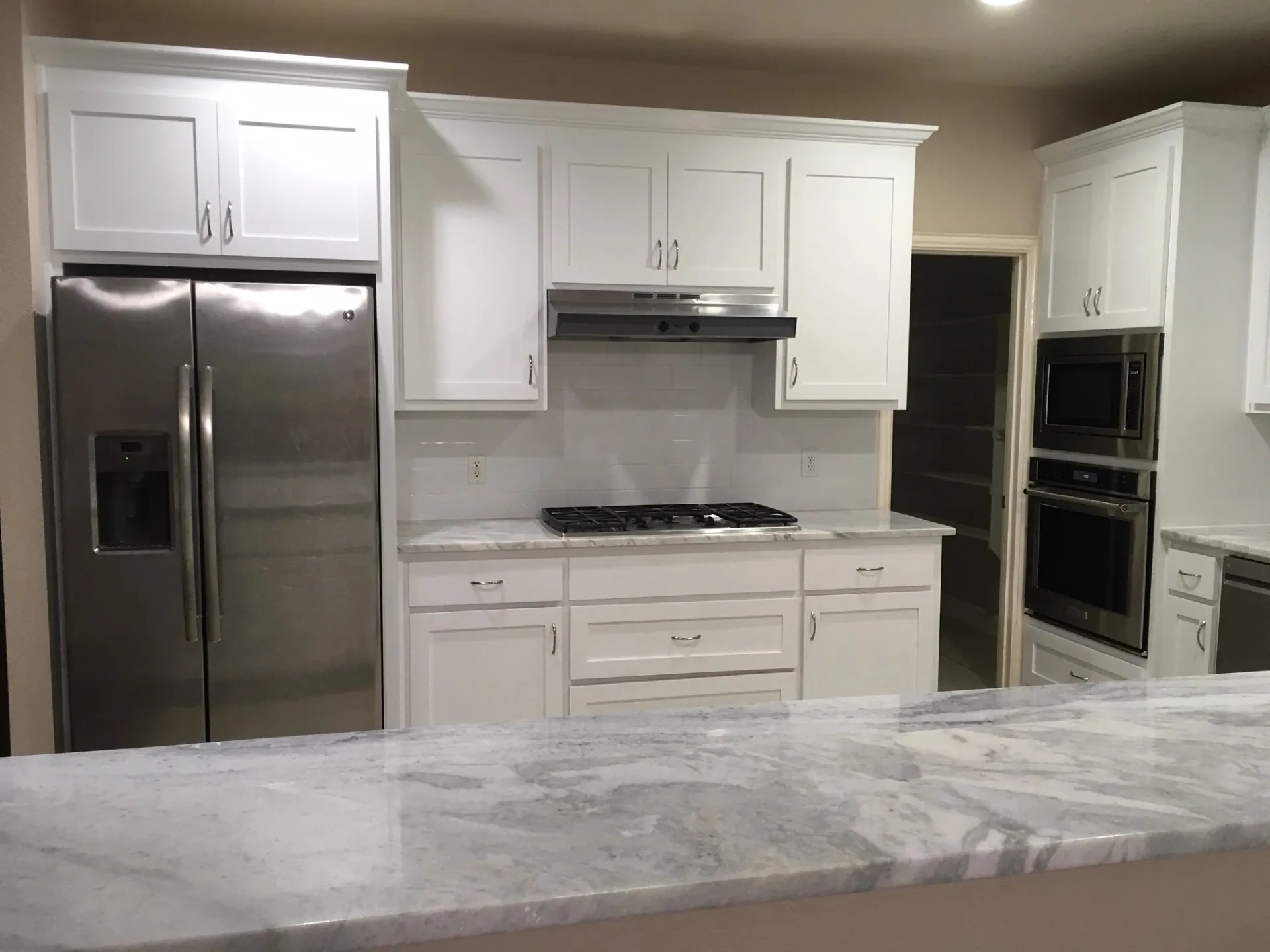 Kitchen with stainless steel appliances, light stone counters, and white cabinetry