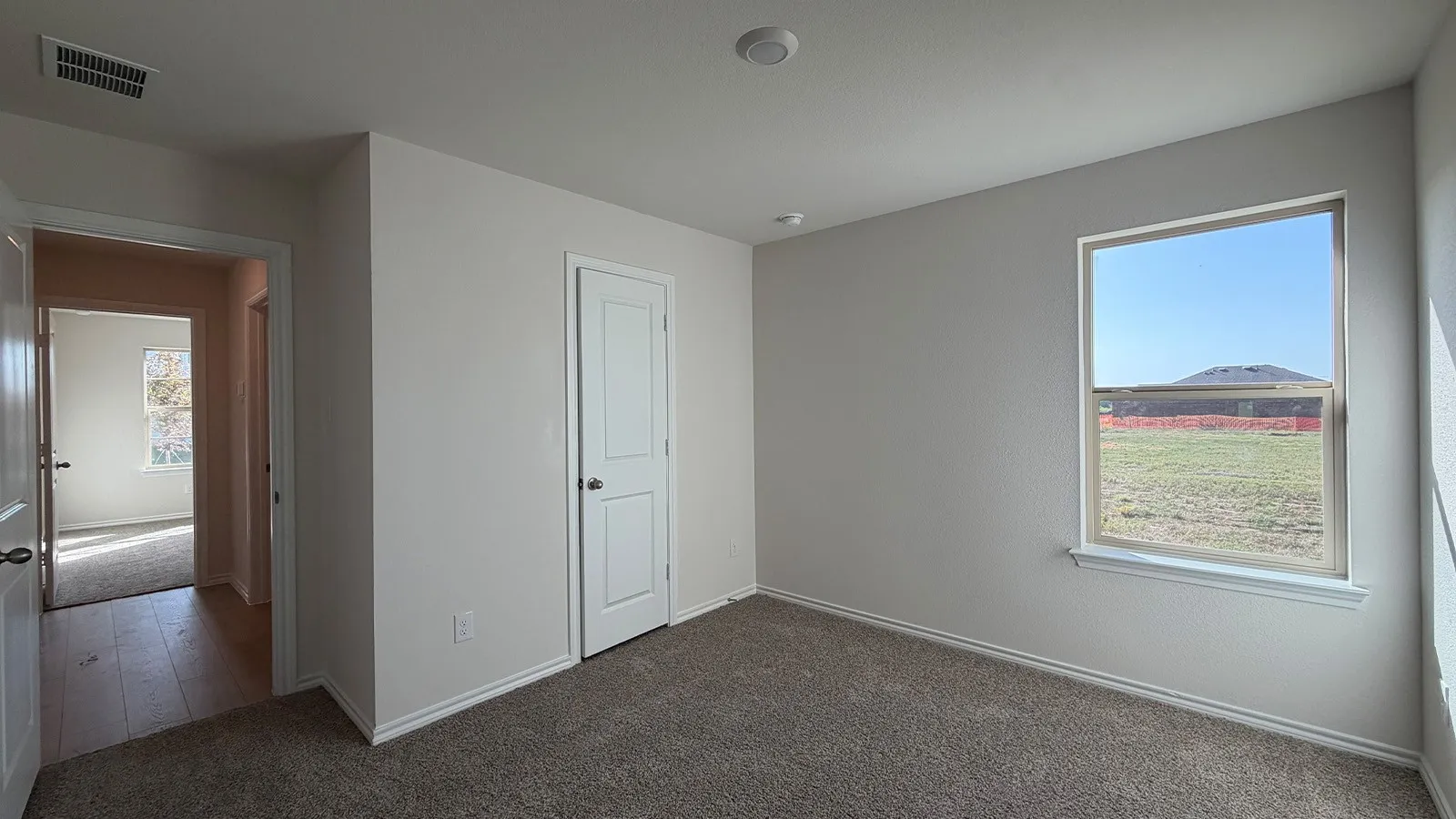 Carpeted bedroom with a single window, white trim throughout, and a white interior door