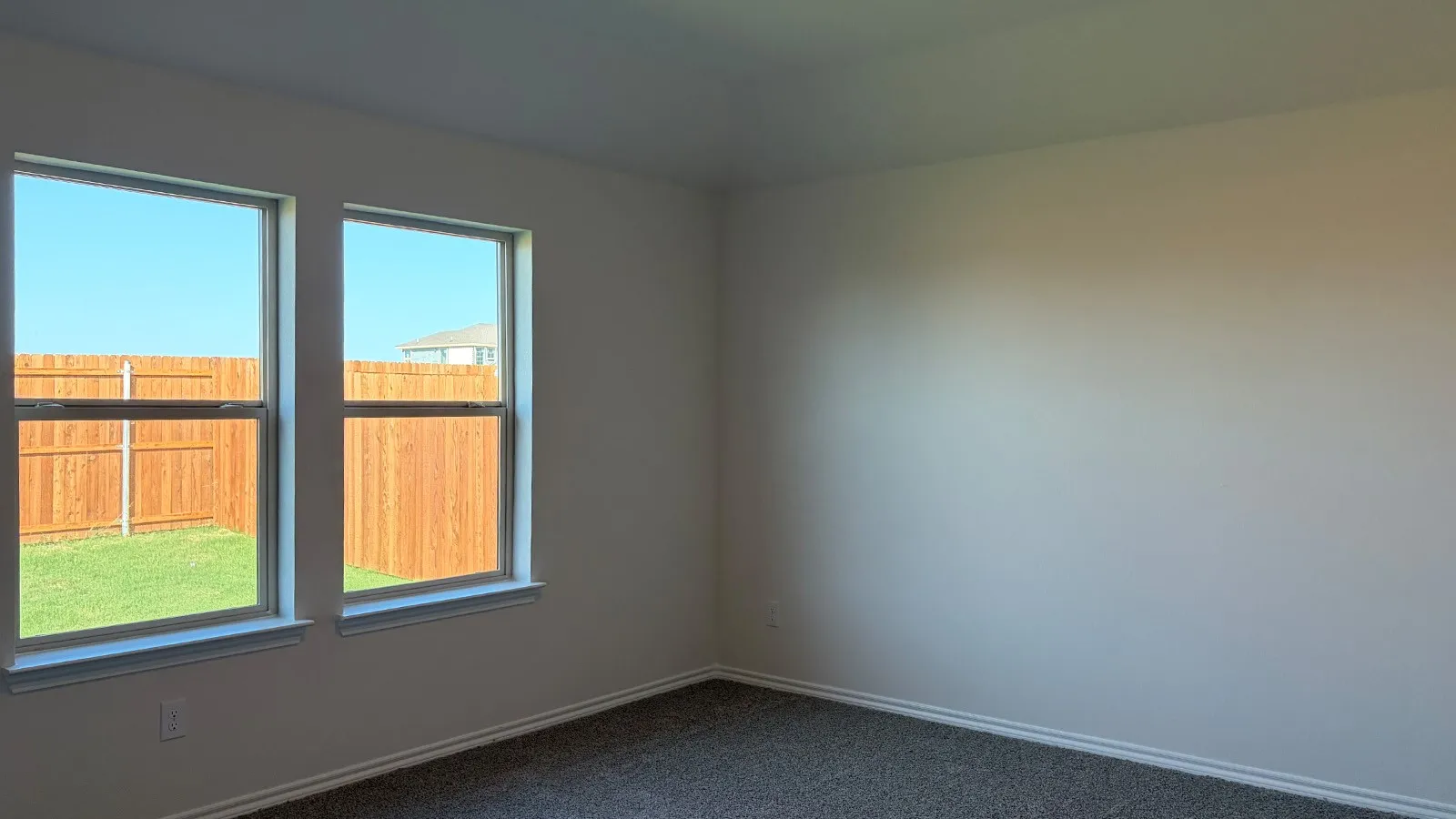 Interior room featuring two double-hung windows, carpet flooring, baseboard molding, and a neutral wall color