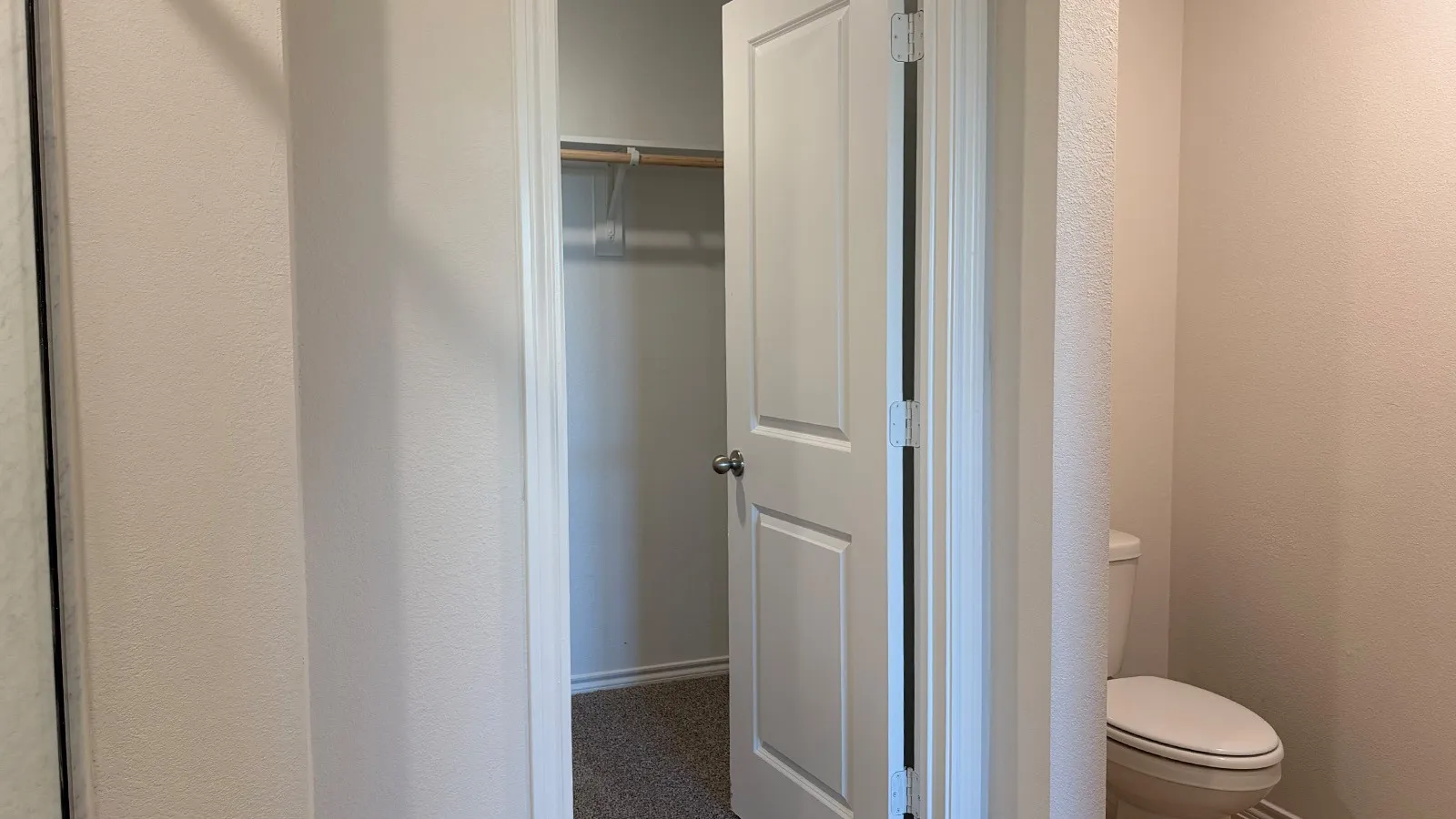 Carpeted closet with a single hanging rod and shelf, accompanied by a white paneled door
