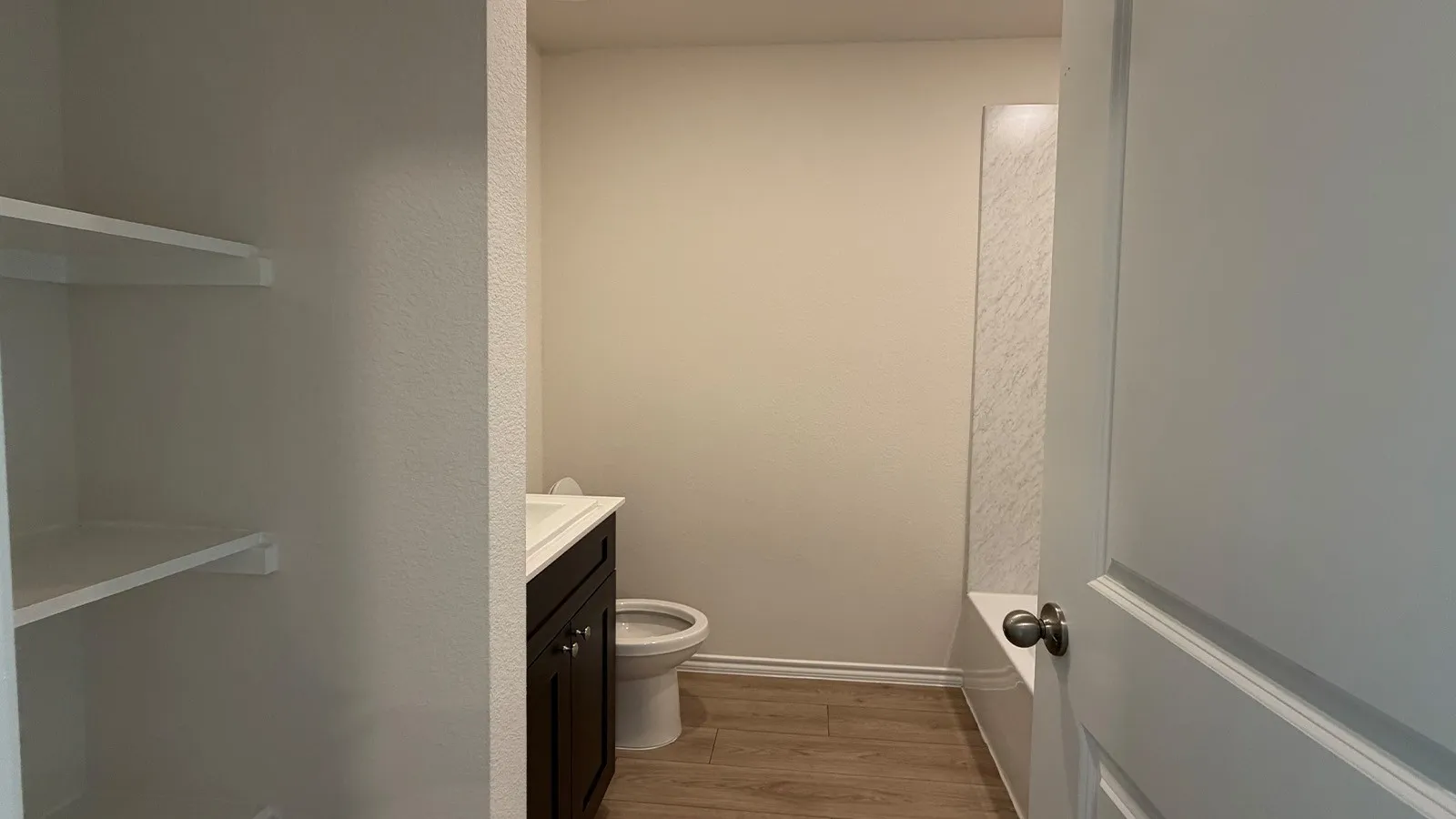 Efficient half bathroom featuring a dark vanity with integrated sink, wood-finish flooring, and white subway tile wainscoting