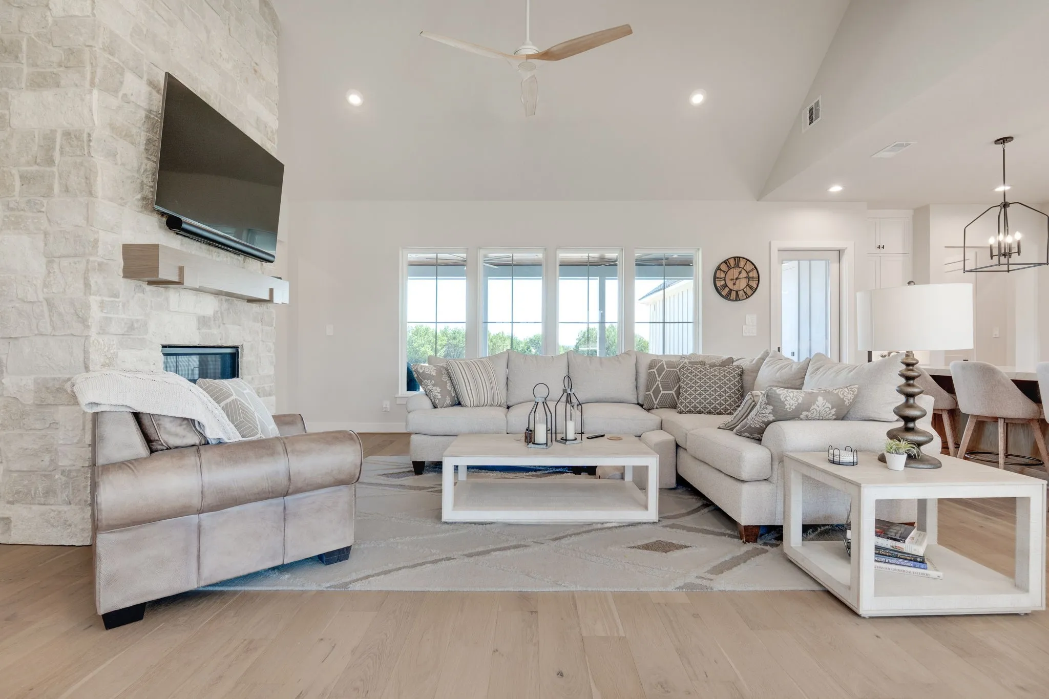 Living room with light wood-style flooring, a ceiling fan, a stone fireplace, hanging lights, and lofted ceiling