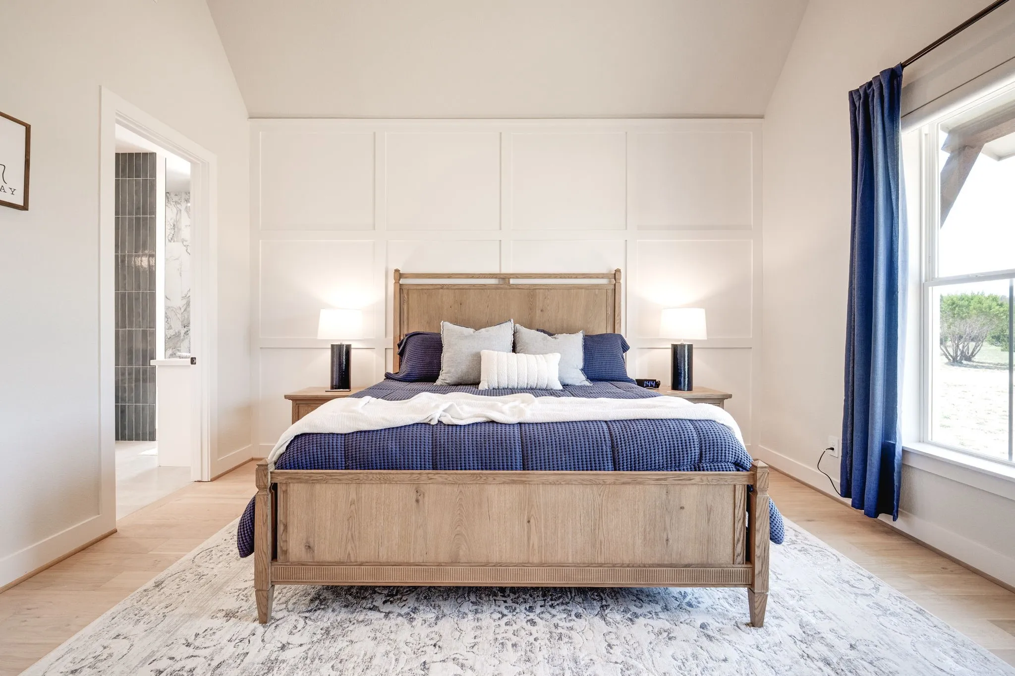 Bedroom with vaulted ceiling, wood finished floors, a decorative wall, and connected bathroom