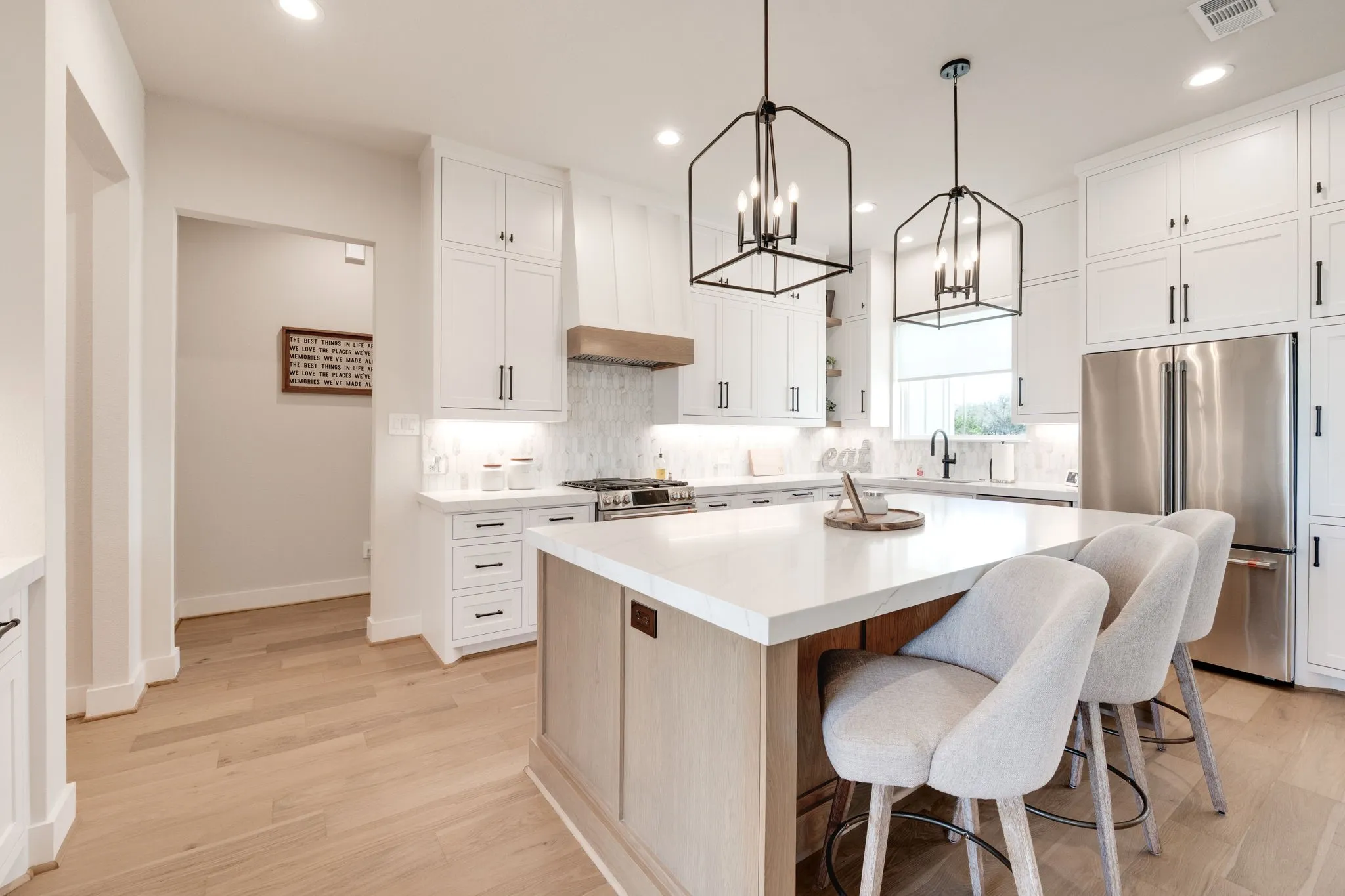 Dual tone kitchen with premium appliances, decorative backsplash, suspended lighting, light wood finished floors, and dual tone cabinetry