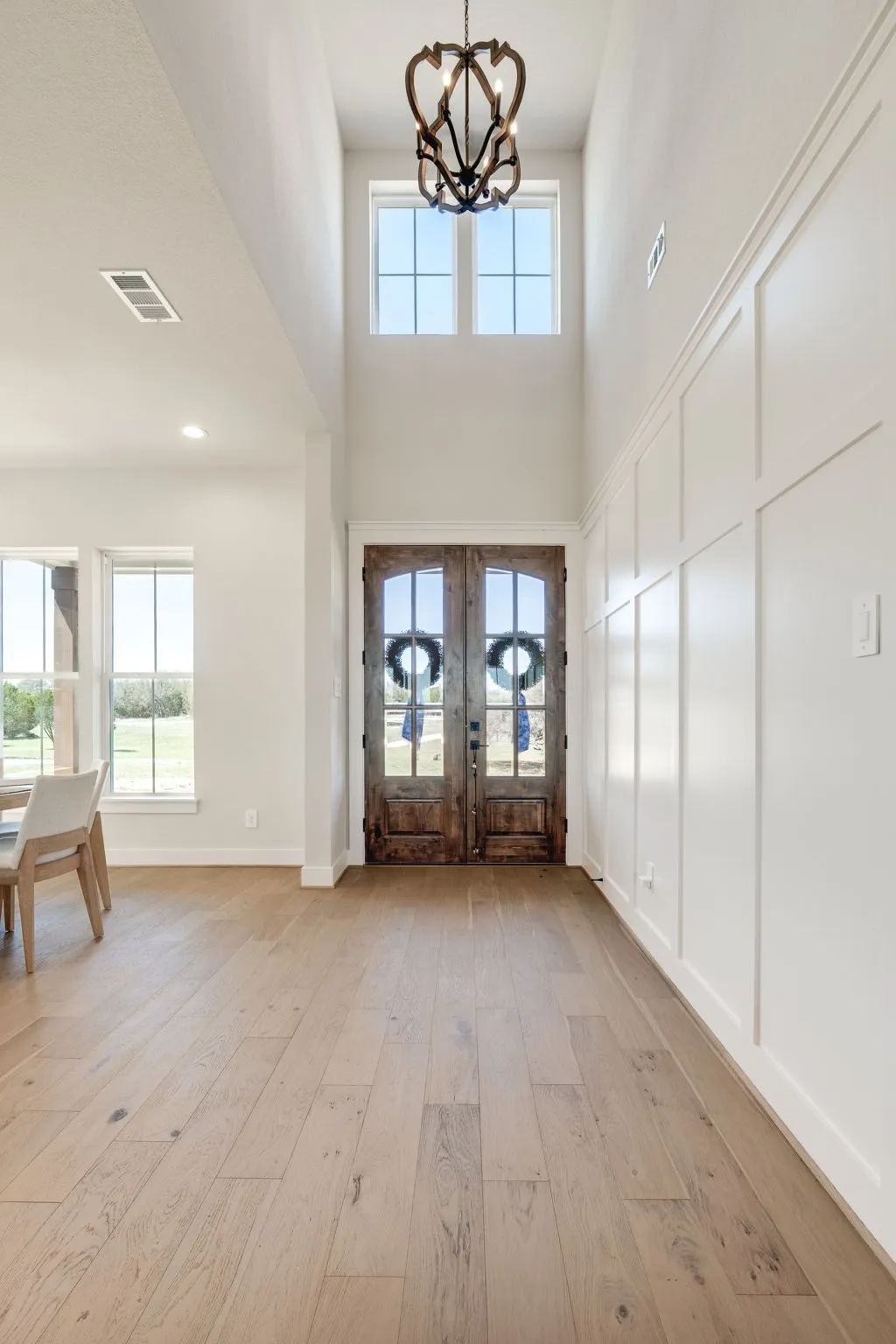 Foyer with light wood-type flooring, french doors, suspended lighting, plenty of natural light, and a high ceiling