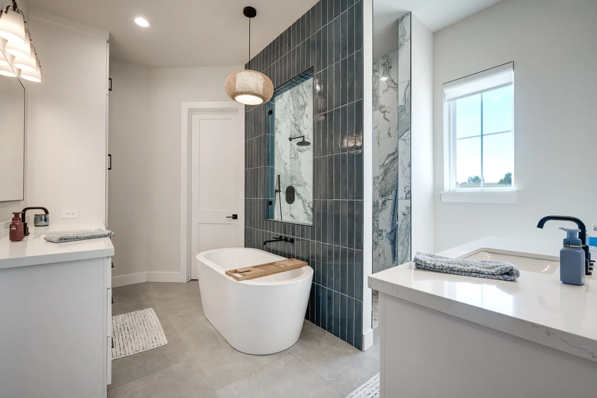 Bathroom featuring two vanities, a freestanding tub, walk in shower, and light tile patterned floors