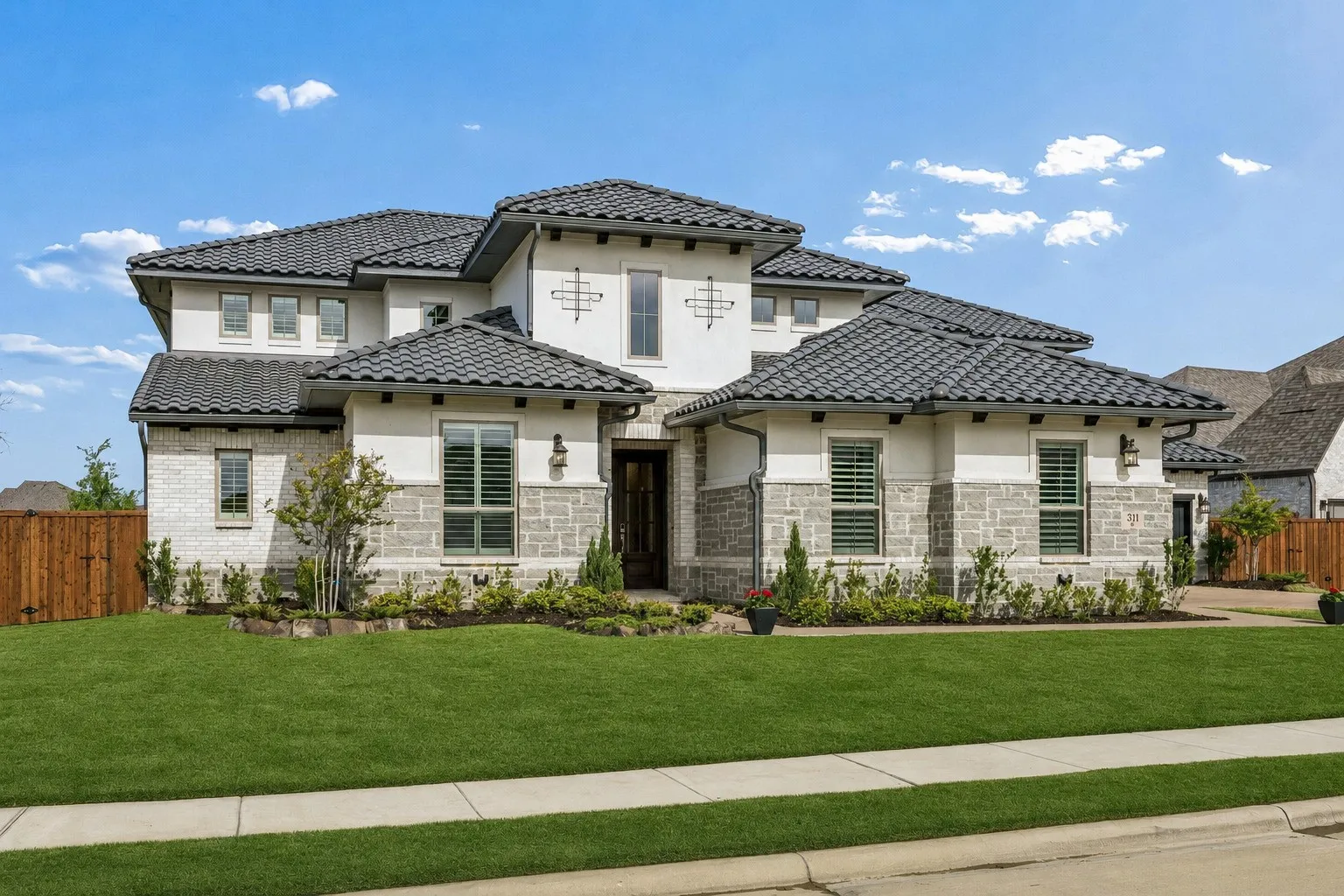 Mediterranean-style exterior featuring a multi-level tile roof, light-colored stone accents, stucco siding, and a dark wood entry door