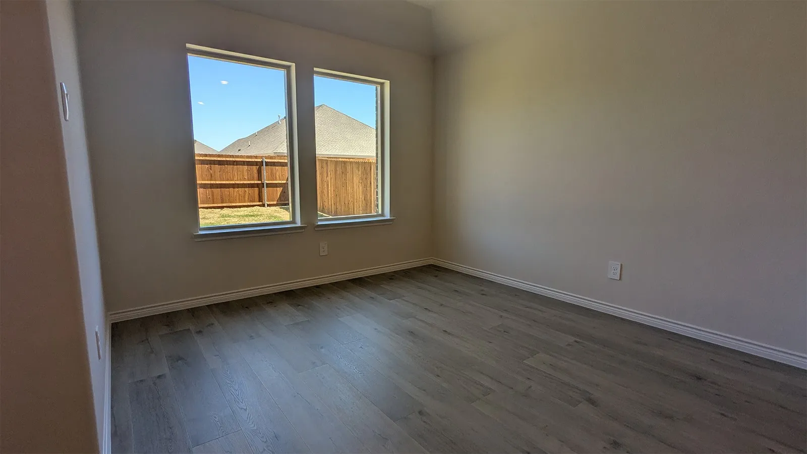 Room featuring two windows, light-toned walls, and wood-finish flooring