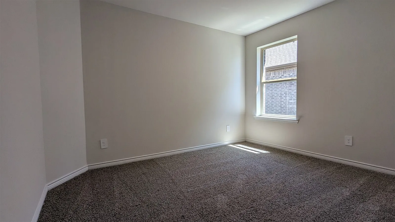 Neutral-toned walls complement the textured gray carpet in this room featuring a single window with white trim
