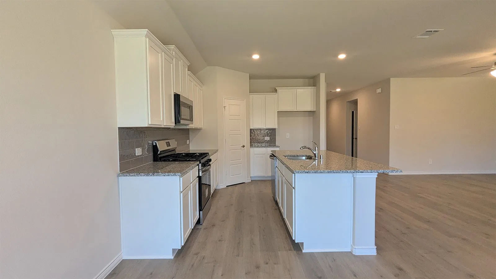 Modern kitchen featuring white cabinetry, granite countertops, a tile backsplash, stainless steel appliances, and wood-finish flooring