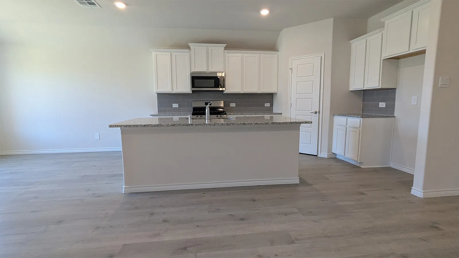 Kitchen featuring a central island with a speckled countertop, white cabinetry with silver-tone hardware, an undermount sink with a gooseneck faucet, a subway tile backsplash, and wood-finish flooring