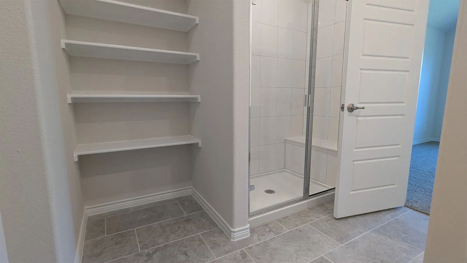 Spacious walk-in shower with a built-in bench and glass enclosure, complemented by extensive built-in shelving, tile flooring, and a modern five-panel interior door