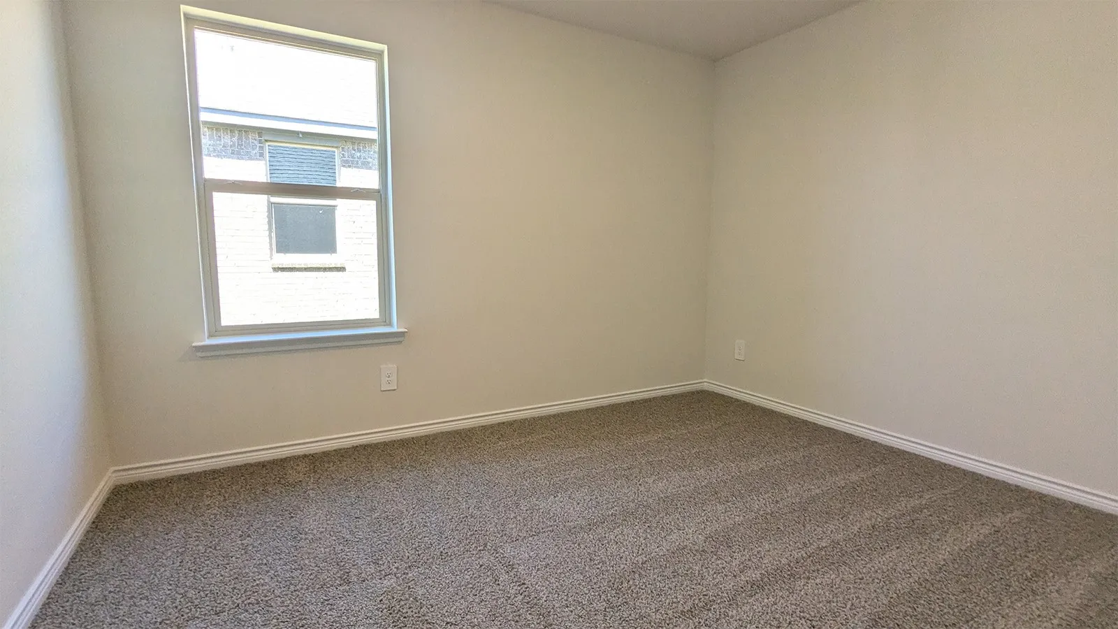 Neutral tone wall paint with white trim, a single window, and textured gray carpet