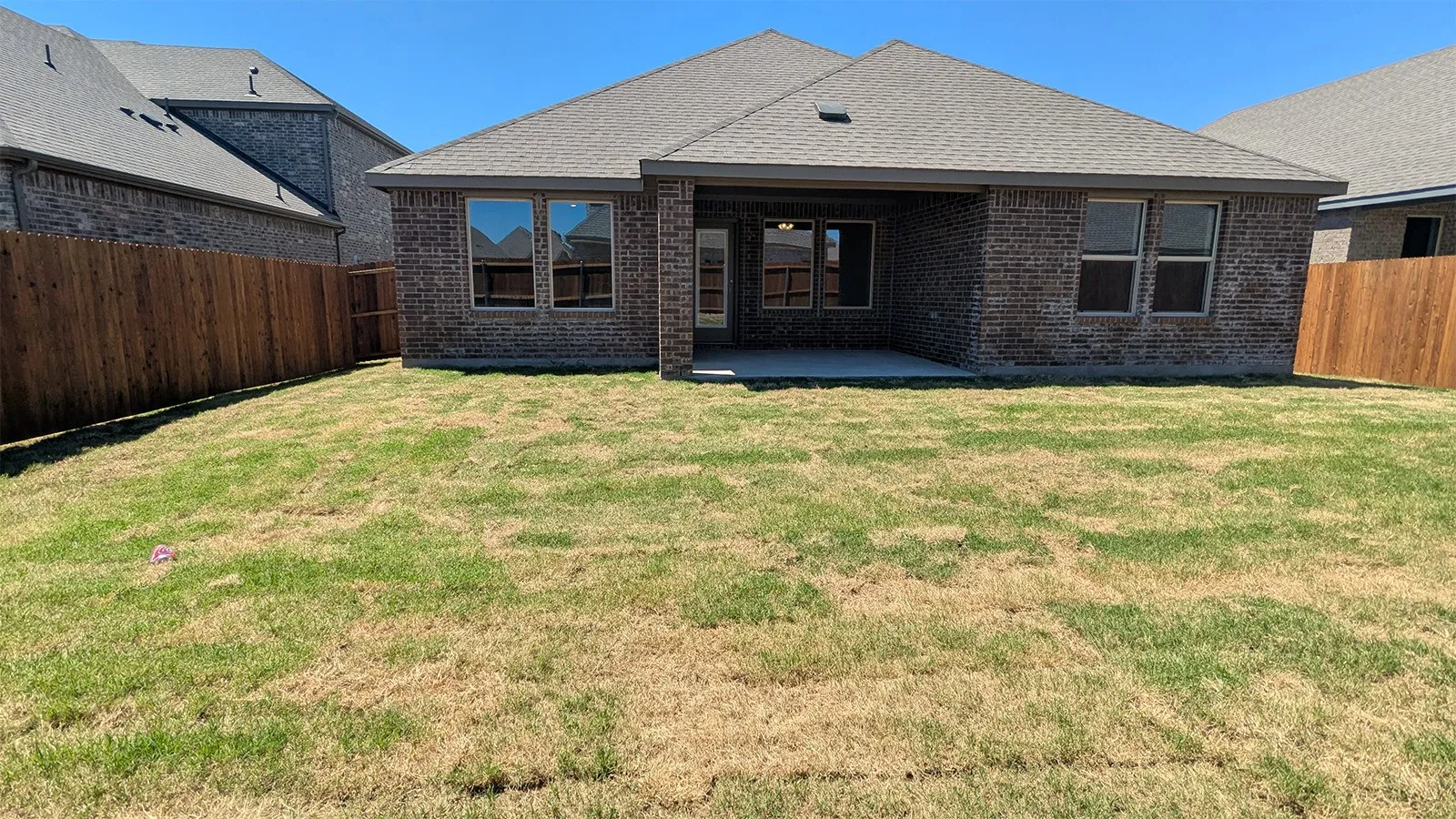 Expansive backyard featuring a covered patio, brick exterior, wood privacy fencing, and multiple windows
