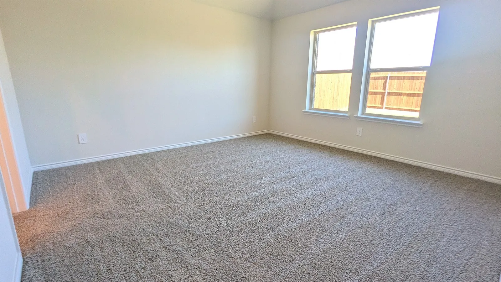 Carpeted interior space featuring two windows with white trim, light-colored walls, and white baseboards