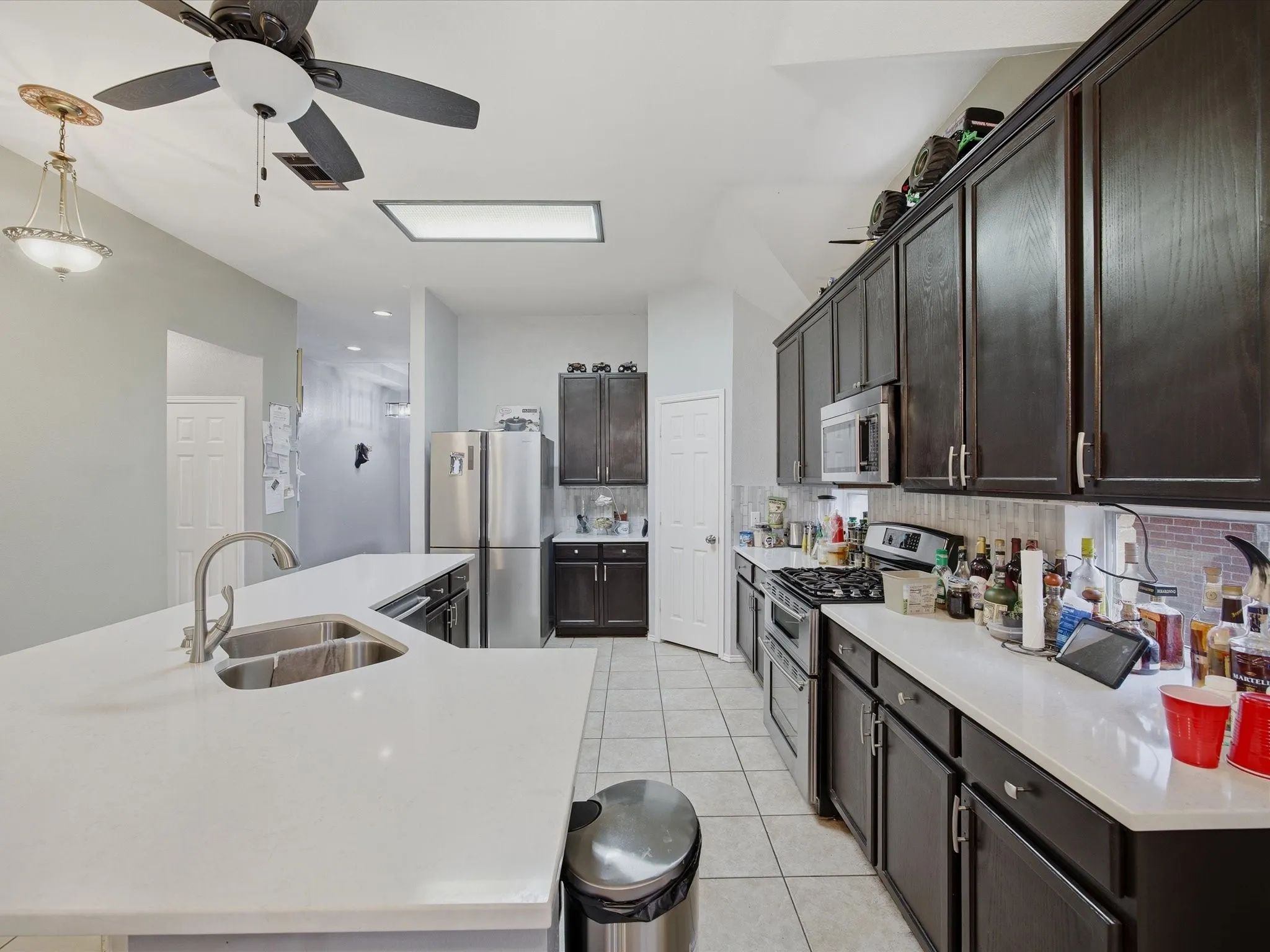 Kitchen featuring stainless steel appliances, a large island, light tile patterned floors, dark wood finish cabinets, and a ceiling fan