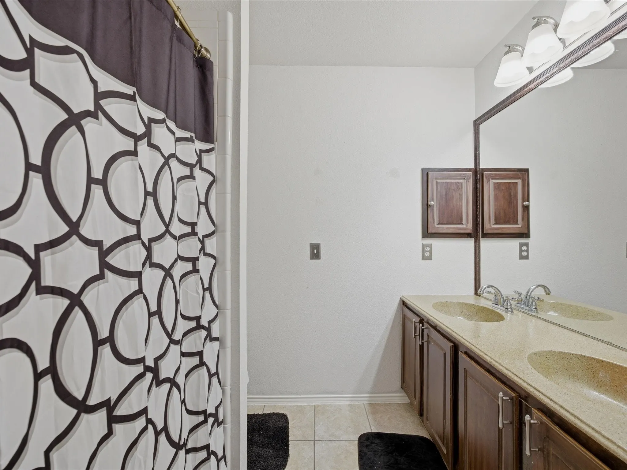 Bathroom with double vanity, curtained shower, and light tile patterned floors
