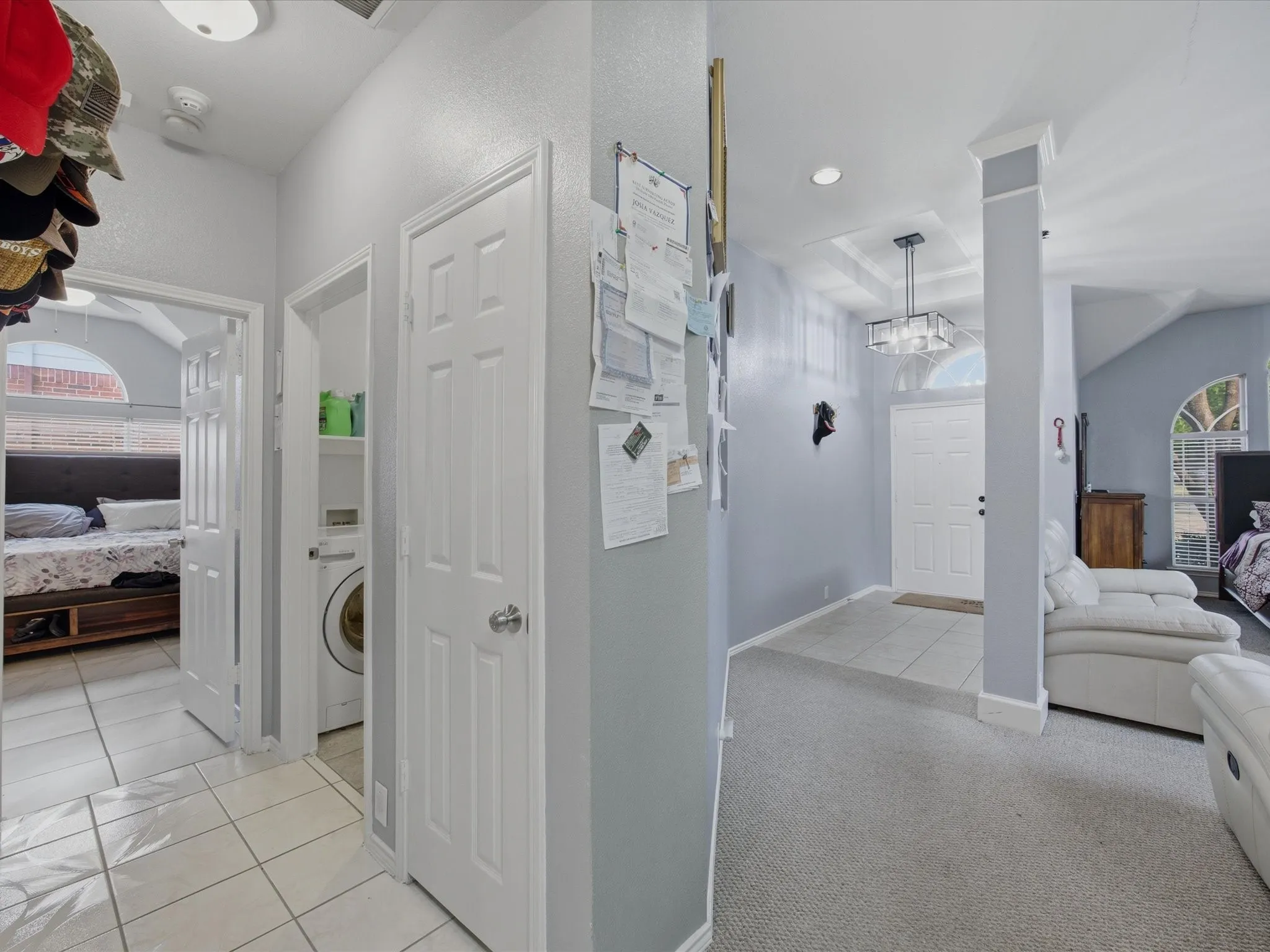 Corridor with healthy amount of natural light, washer / clothes dryer, light carpet, light tile patterned floors, and a raised ceiling