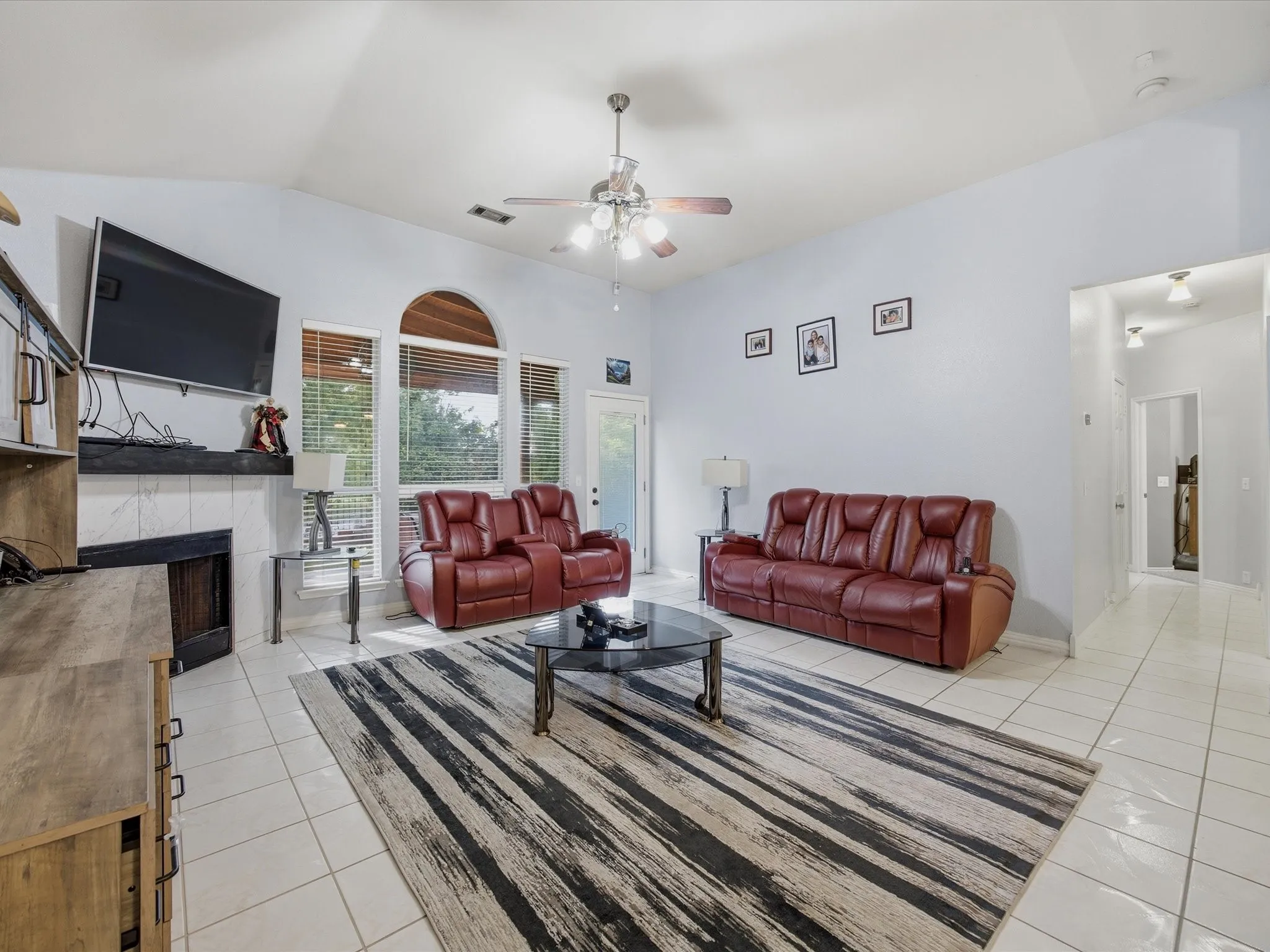 Living area with ceiling fan, vaulted ceiling, a fireplace, and light tile patterned floors