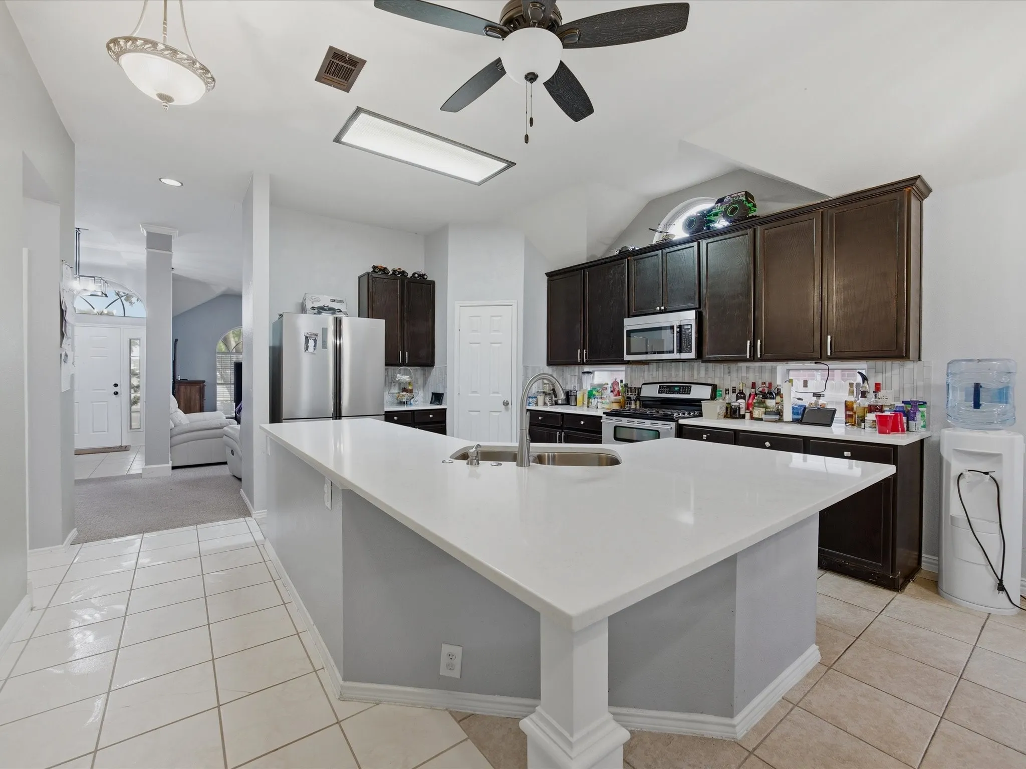 Kitchen with dark wood finish cabinetry, ceiling fan, stainless steel appliances, vaulted ceiling, and a large island with sink