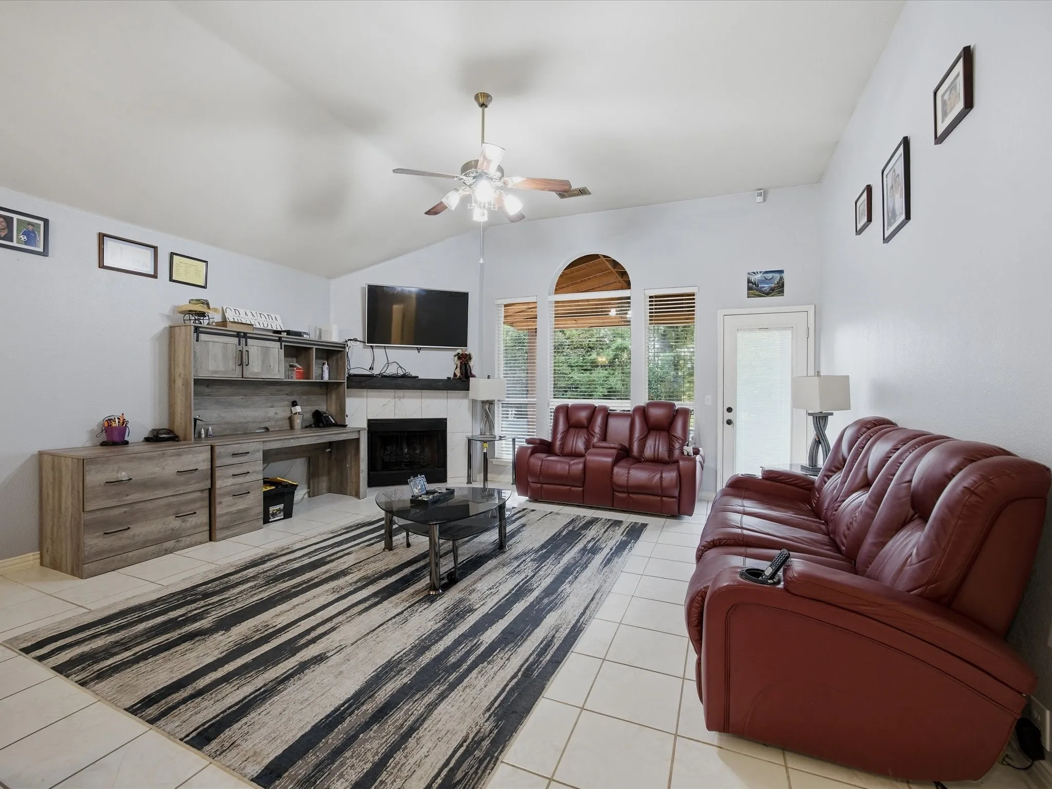 Living area featuring a tile fireplace, light tile patterned floors, ceiling fan, and vaulted ceiling